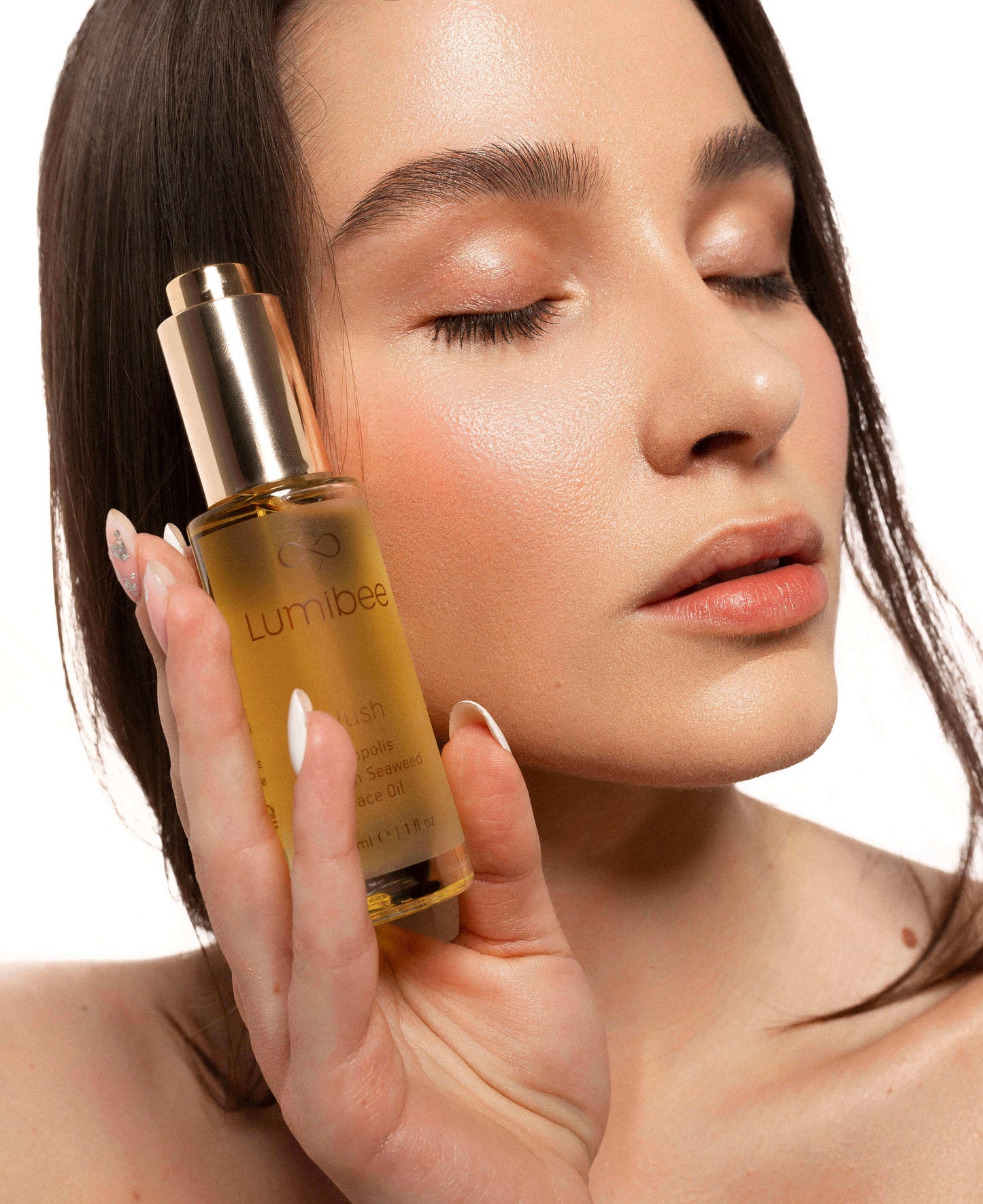 A girl holding a face oil close to her skin.